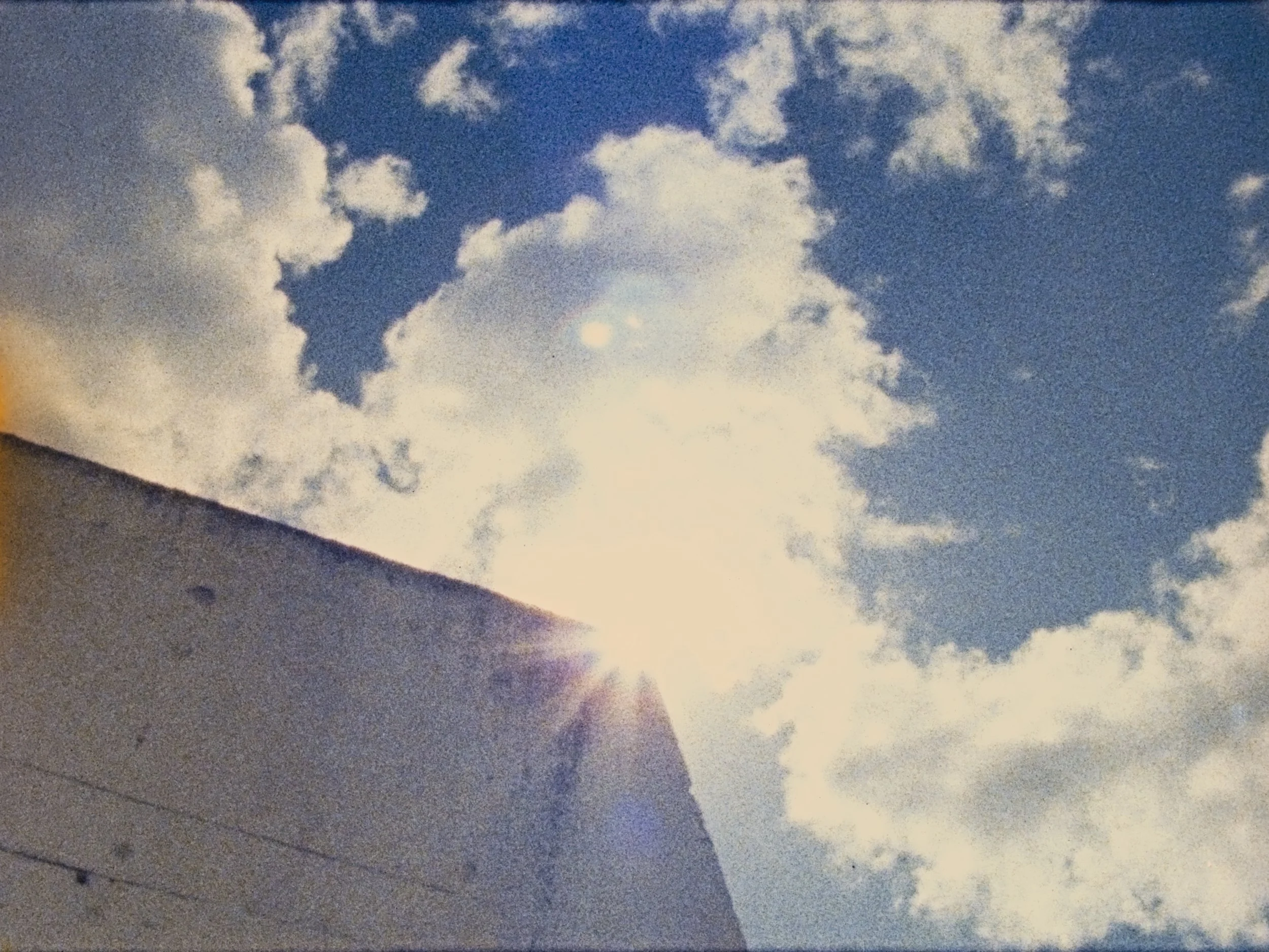 Cloudy sky with the sun peeking from behind a building, creating a lens flare effect.