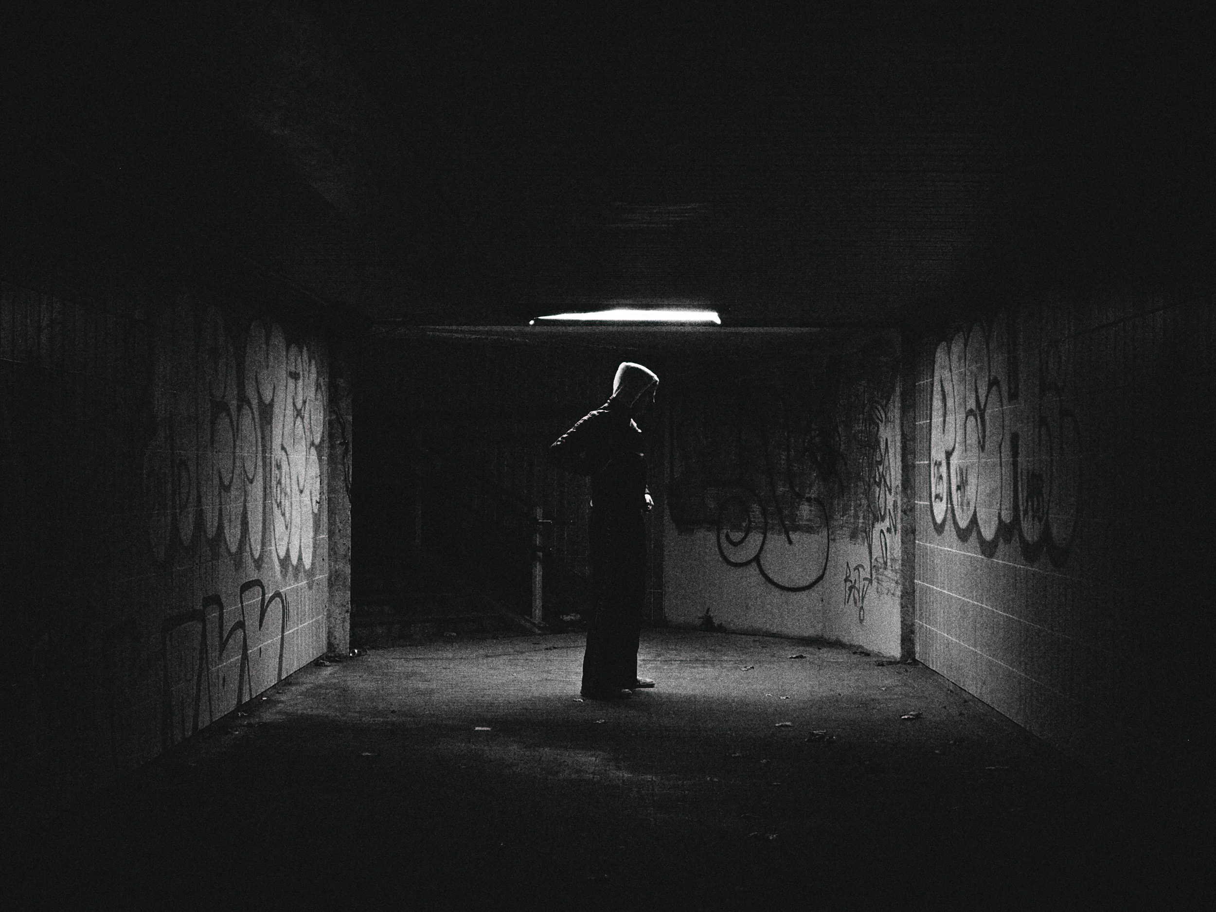 Silhouette of a person standing in a graffiti-covered underpass with a light coming from above.