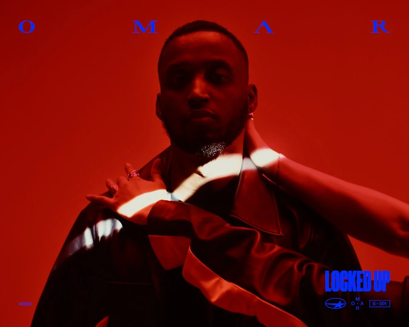 A man with dark skin and short hair standing against a red background, looking at the camera. He is wearing a dark jacket, and a hand is resting on his shoulder. The text 'OMAR' appears in blue at the top, and 'LOCKED UP' with a subtext 'MOAR' and so