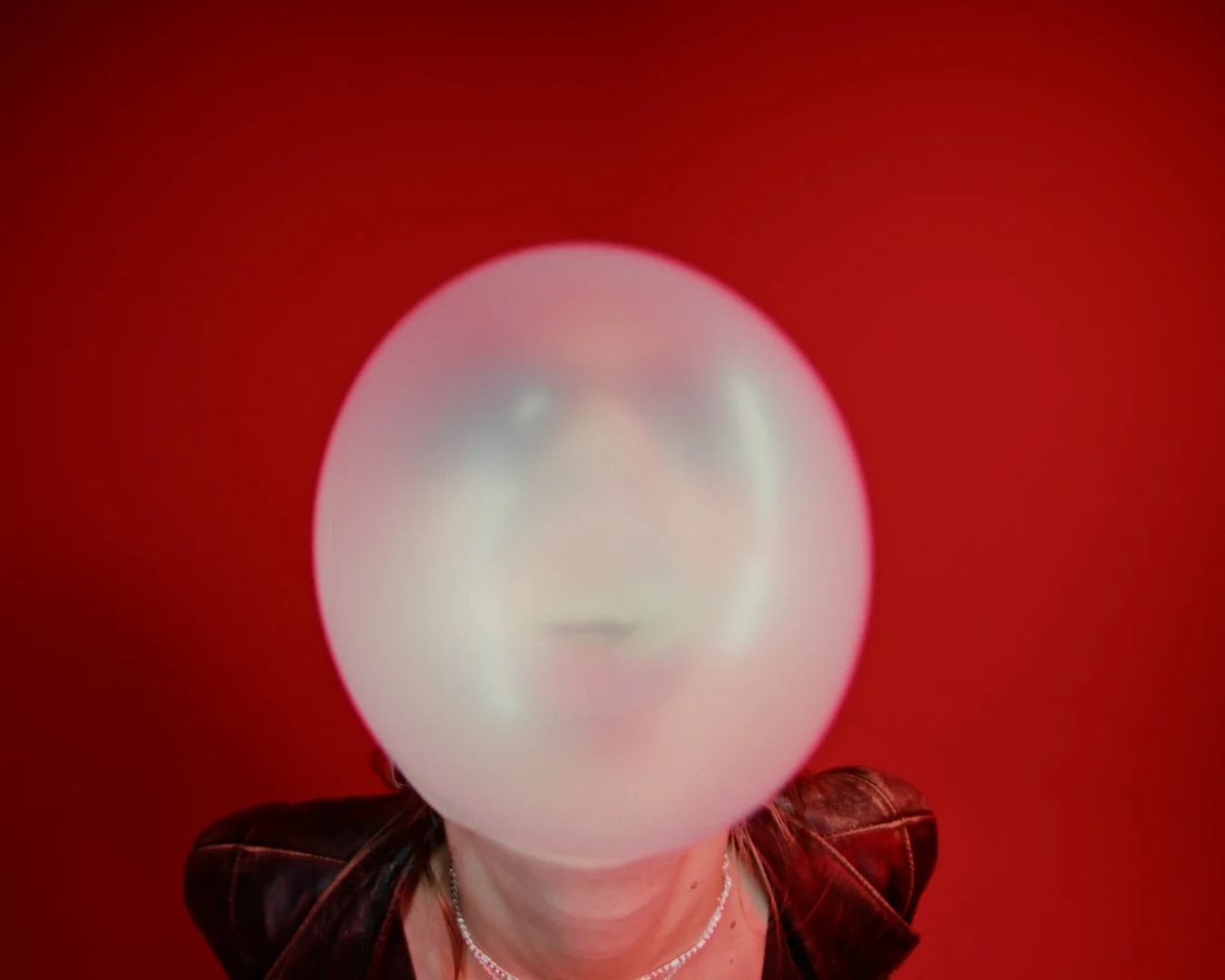 Person with a large white ball covering their face against a red background.