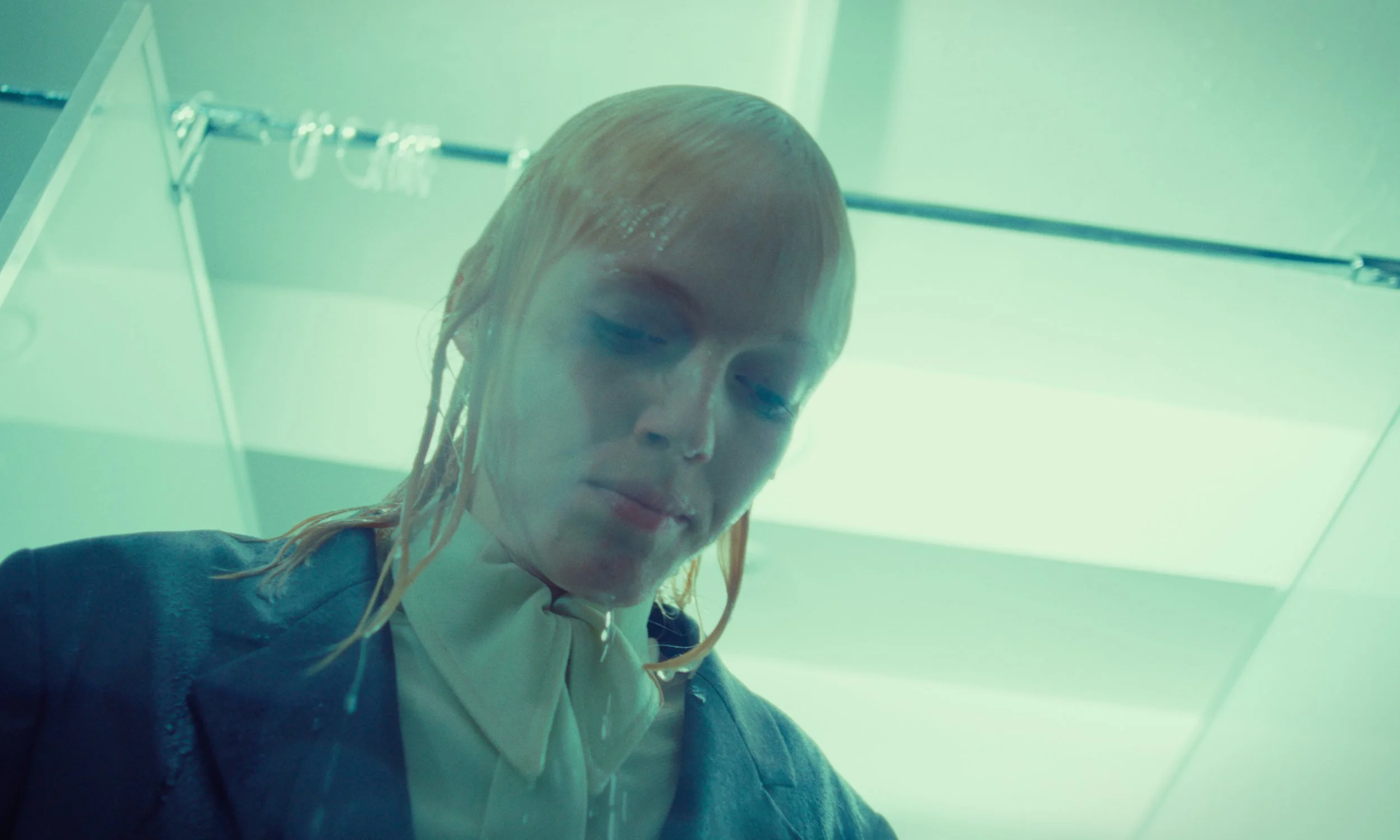 A woman with wet, blonde hair looking down in a setting with green-tinted lighting.
