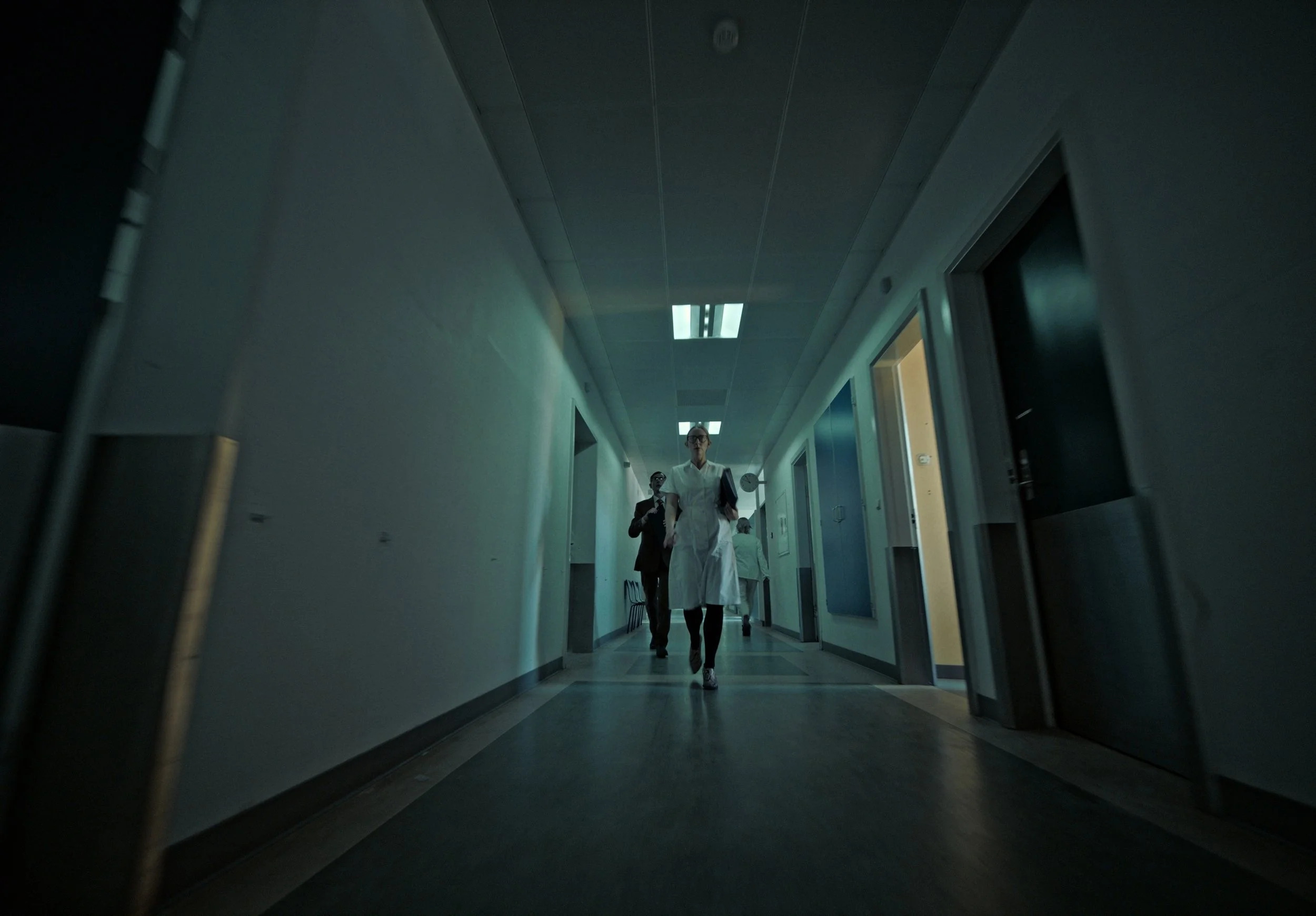 Healthcare professionals walking down a hospital corridor, with a nurse in the foreground and other staff in the background.
