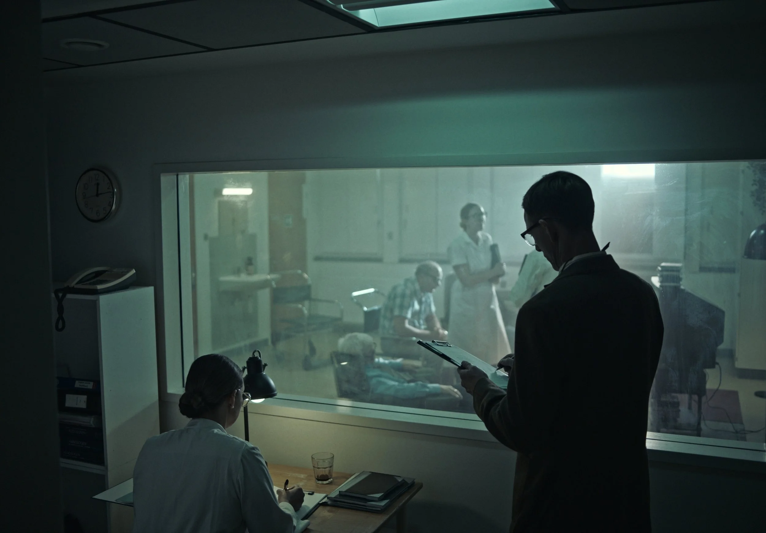 A hospital scene viewed through a glass window showing medical staff and patients. Inside, a woman doctor is writing at a desk, while a man in professional attire reads a clipboard. Outside, patients sit and wait, with one lying in a hospital bed. Me