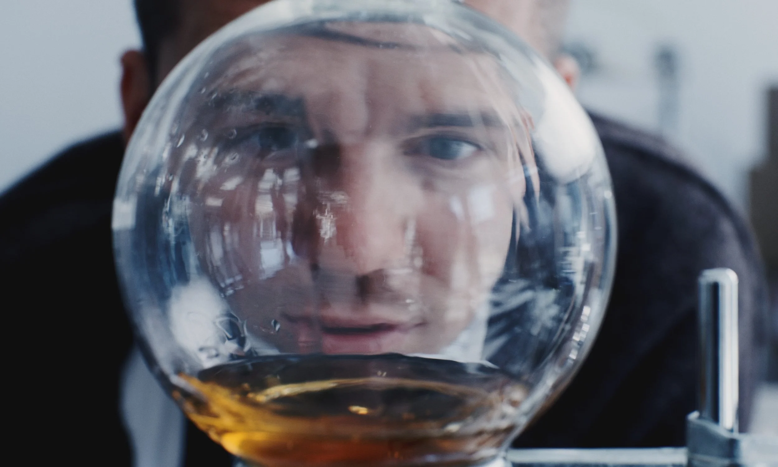 Person looking through a glass bowl with a liquid inside, distorting their face.