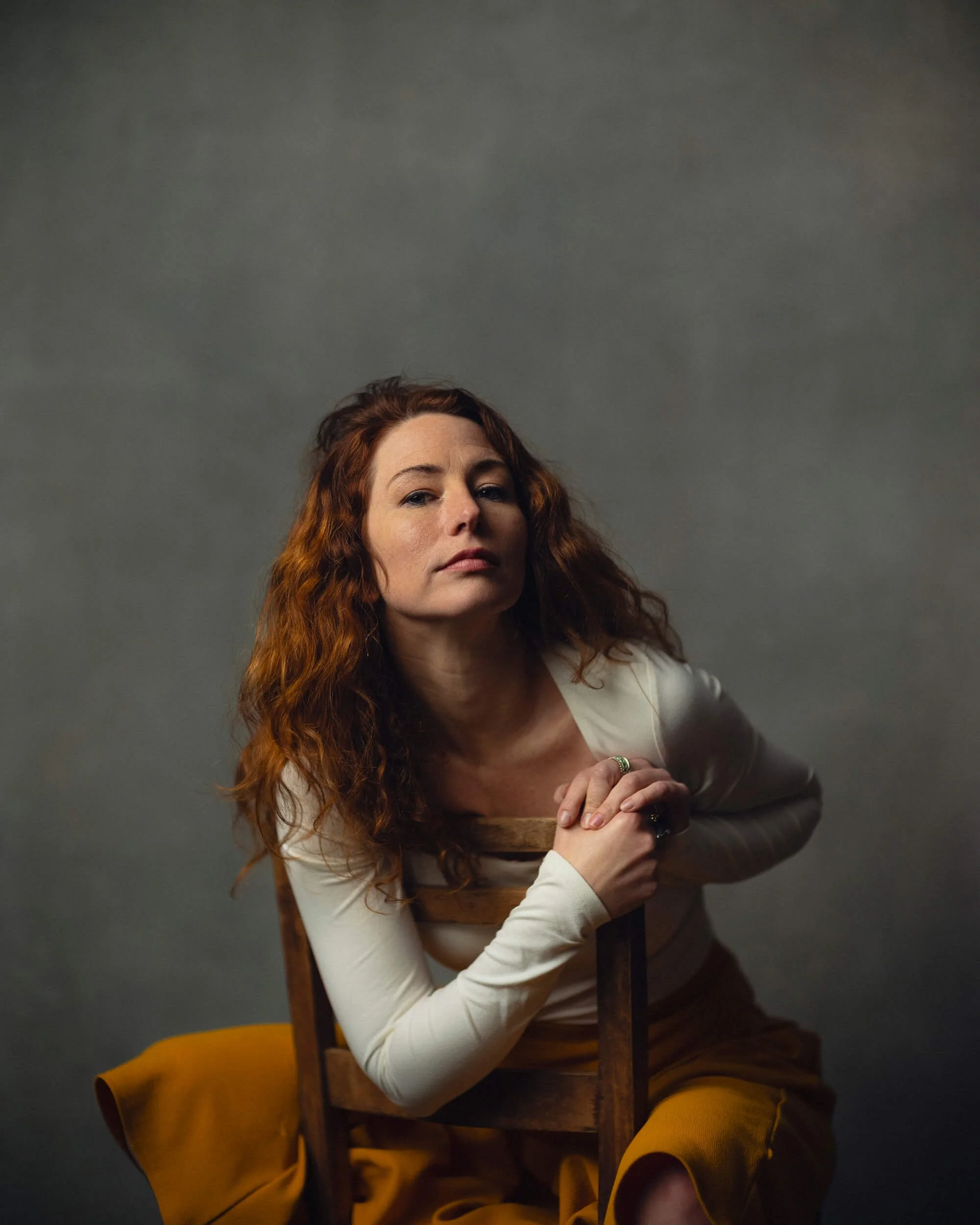 London based Actress sat backwards on a chair wearing yellow skirt and white top for a headshot photoshoot