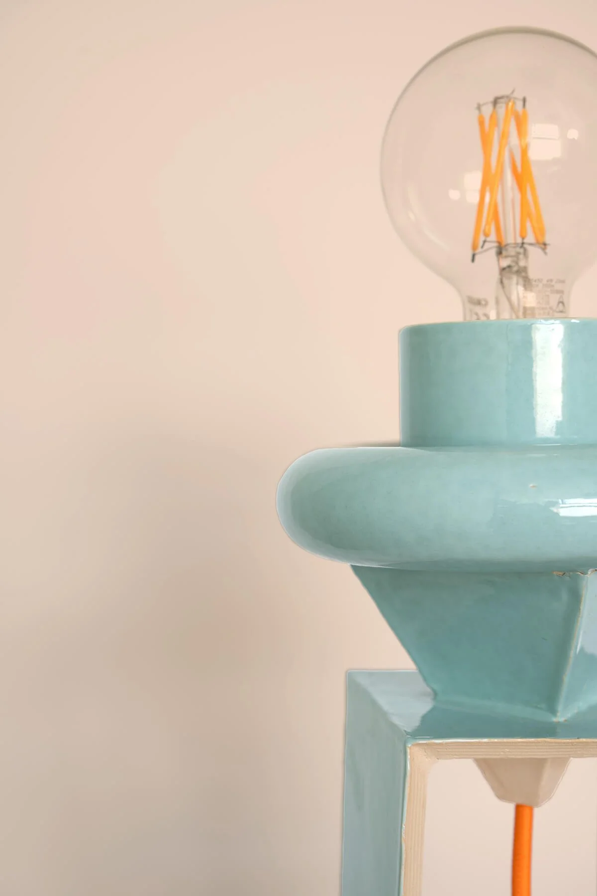 Close-up van een handgemaakte turquoise aardewerk lamp in Memphis-stijl met glanzend glazuur en zichtbare lichtbron, ontworpen in het keramiekatelier LAB L.L. in Vlaardingen.