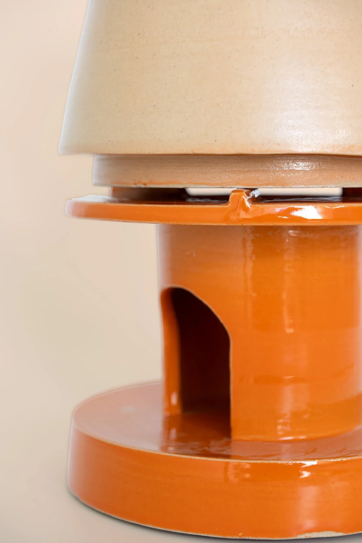 Close-up van het handgemaakte steengoed rechaud met glanzend oranje glazuur en de onderzijde van de theepot van LAB L.L.