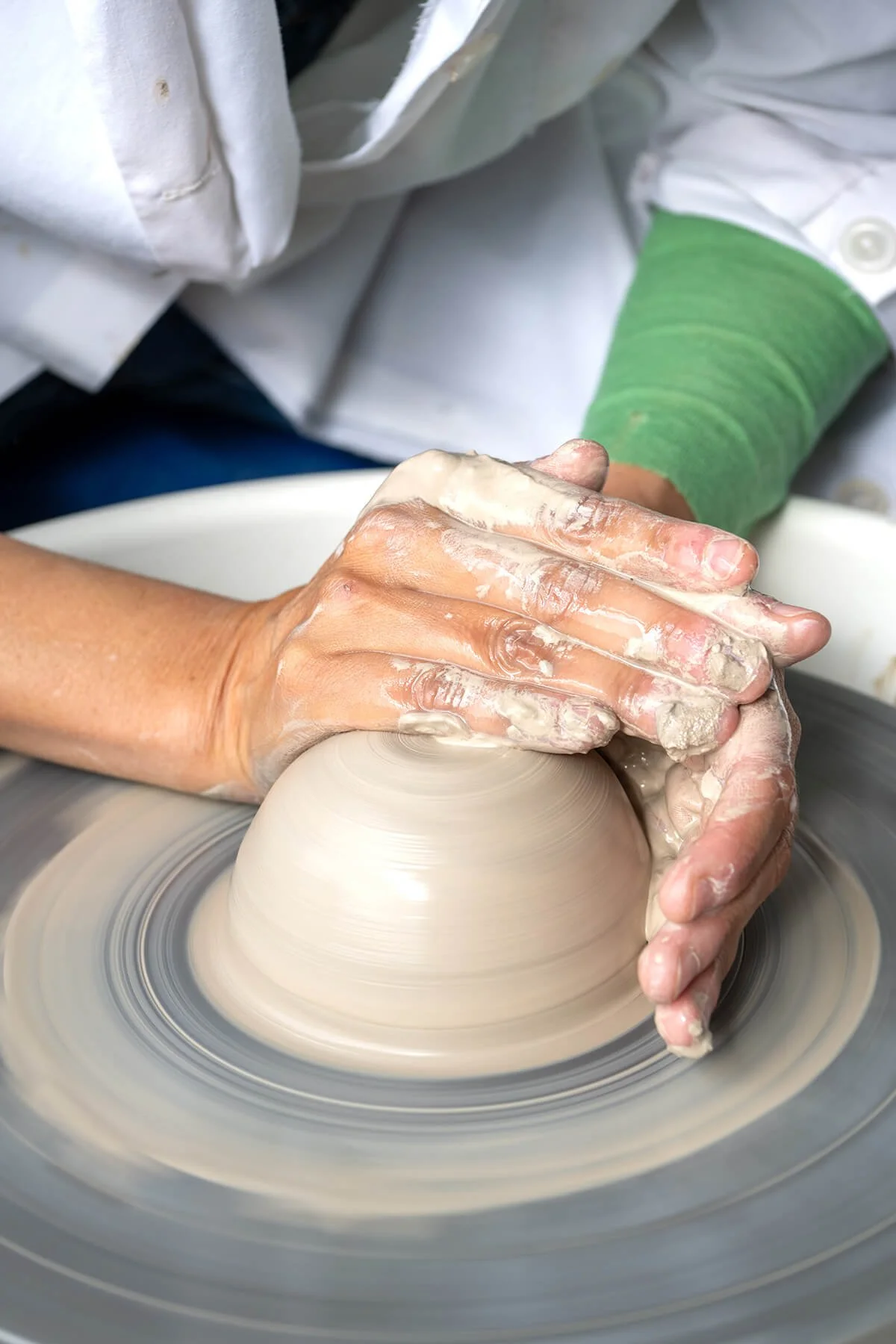 Handen die een kleikom vormen op de draaischijf tijdens een workshop draaien bij LAB L.L., met een spons om de rand te verfijnen.