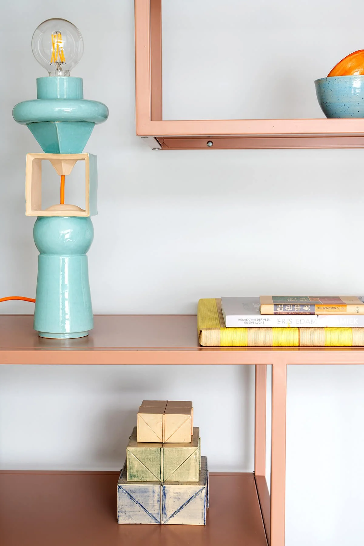 Handgemaakte turquoise keramische lamp in Memphis-stijl, gestyled op een beige-roze wandplank met boeken en keramische objecten in het atelier van LAB L.L. in Vlaardingen.