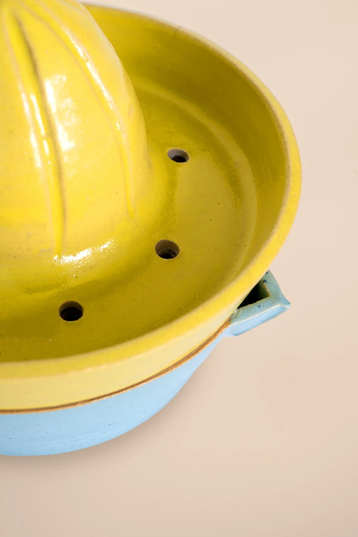 Close-up van een handgemaakte keramieken citruspers in geel en blauw, ontworpen in het keramiekatelier LAB L.L. in Vlaardingen.