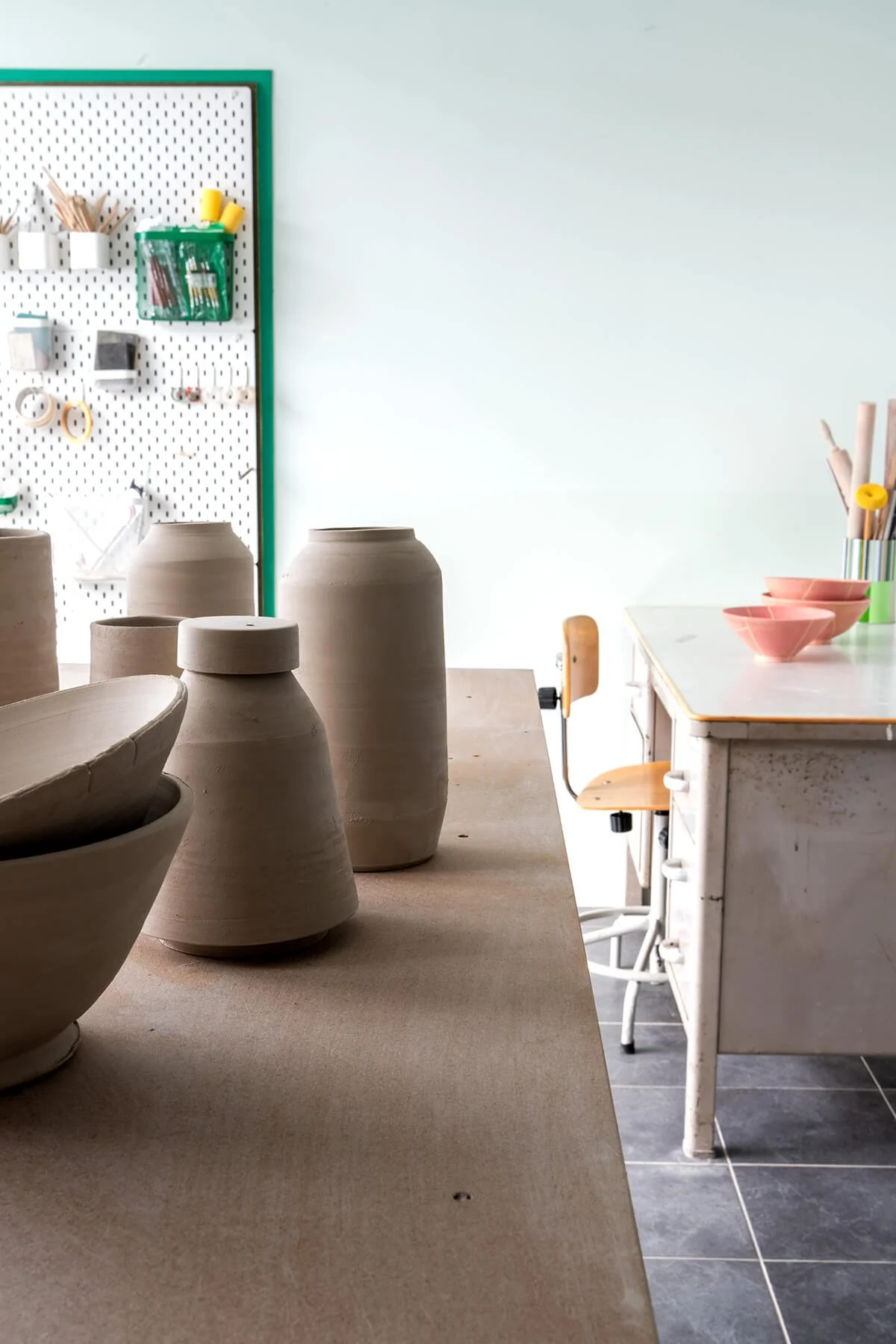 Leerharde keramiekobjecten en schalen op een werktafel in het atelier van LAB L.L., met gereedschappen op een pegboard op de achtergrond.