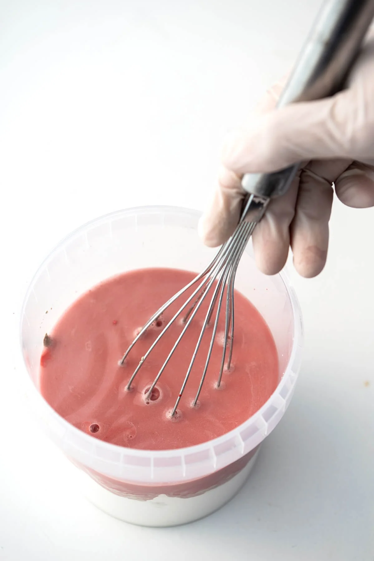 Hand die roze glazuur mengt met een garde in het keramiekatelier van LAB L.L. in Vlaardingen.