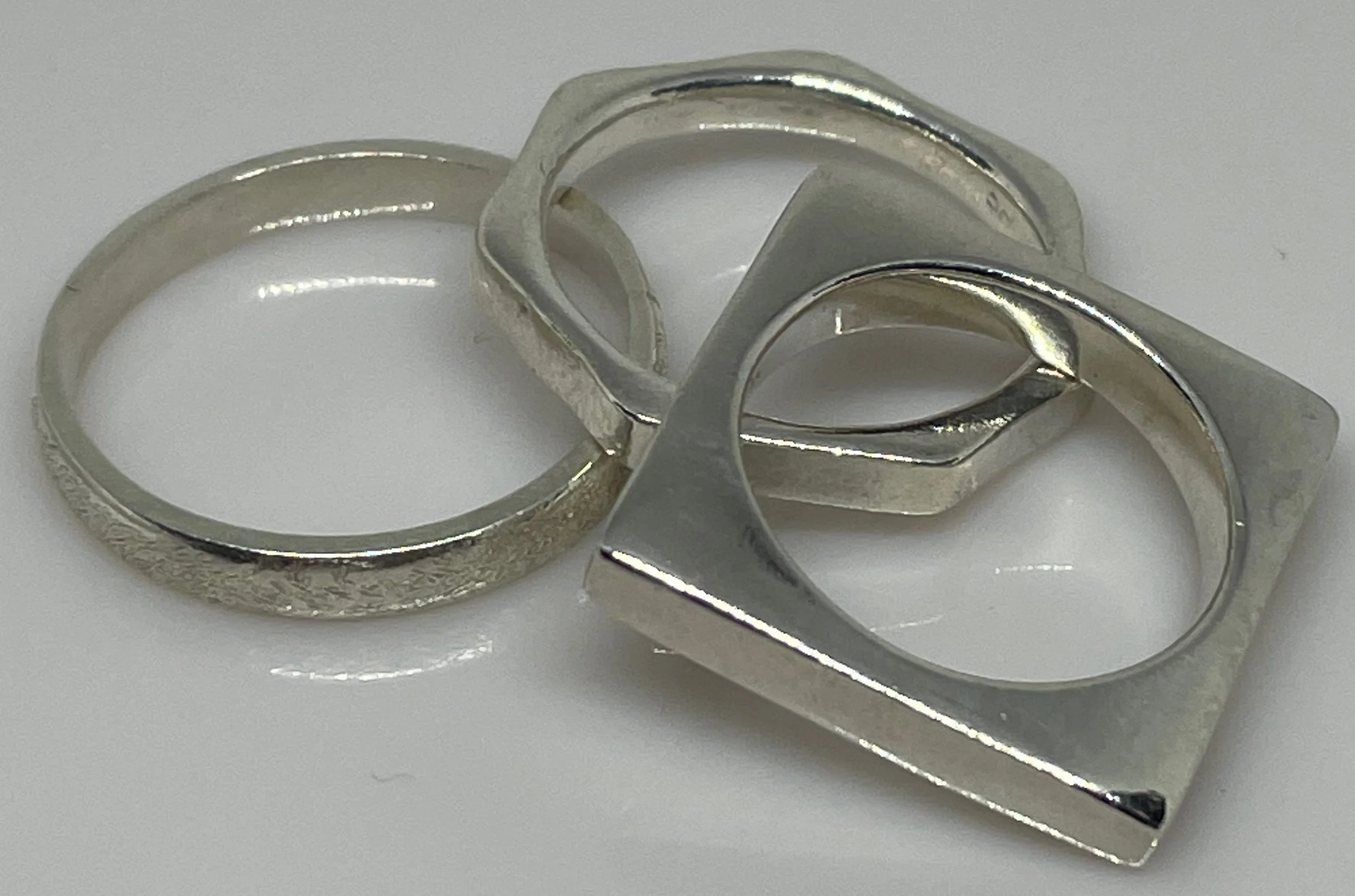 Three silver rings with modern geometric designs on a white surface.