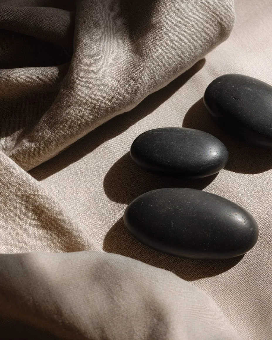 Three smooth black stones placed on a beige fabric surface with a textured brown cloth nearby.