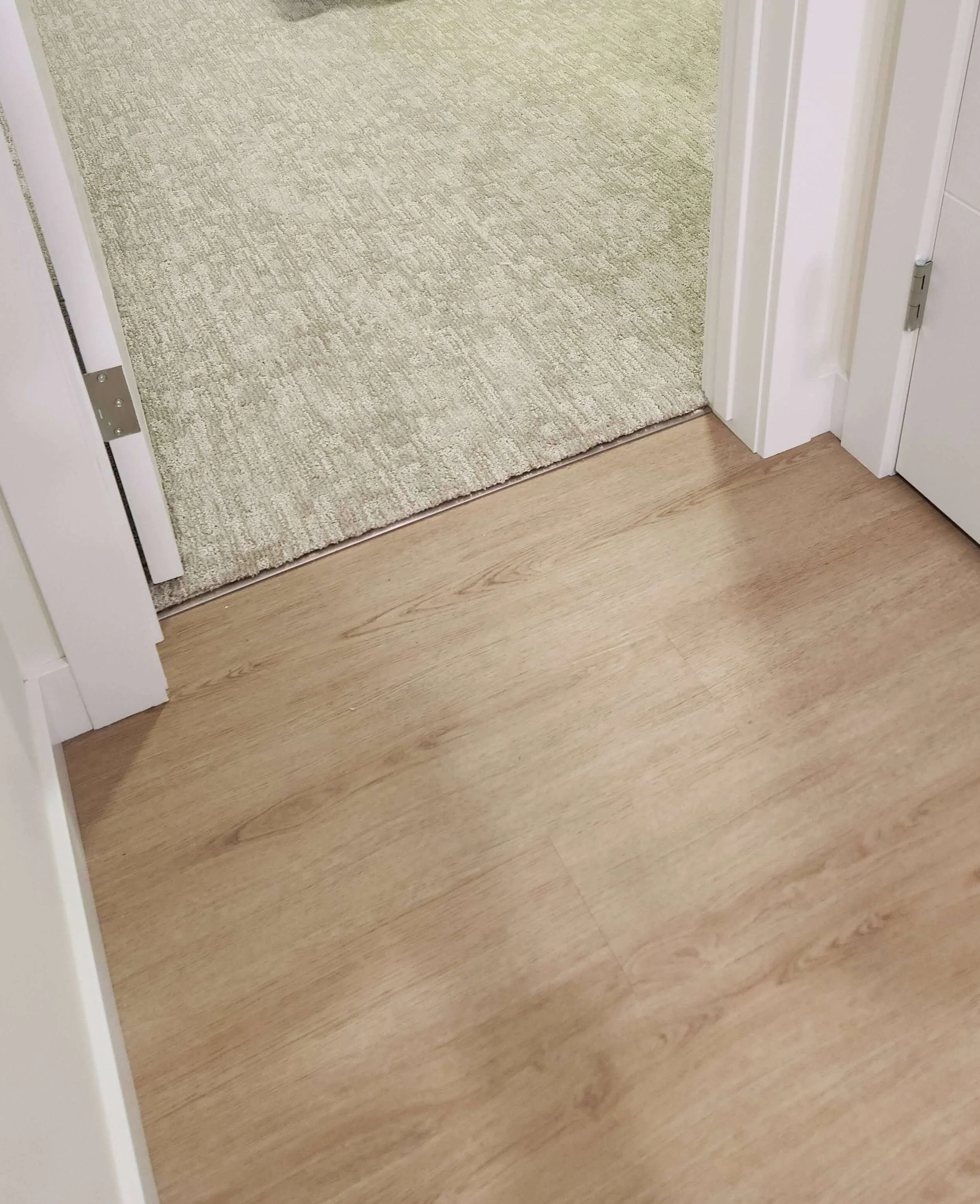 a metal trim bridges the transition from carpet in the bedroom to luxury vinyl plank in the main hallway
