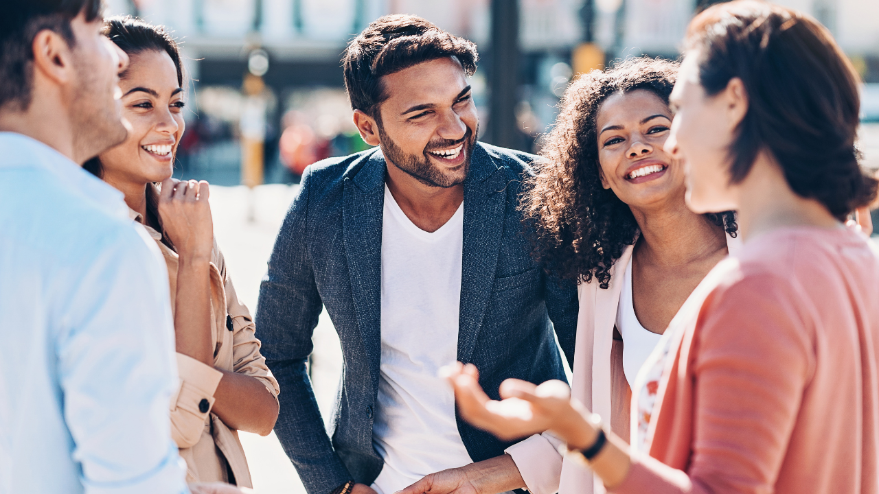Group of five friends laughing and talking outdoors on a sunny day.