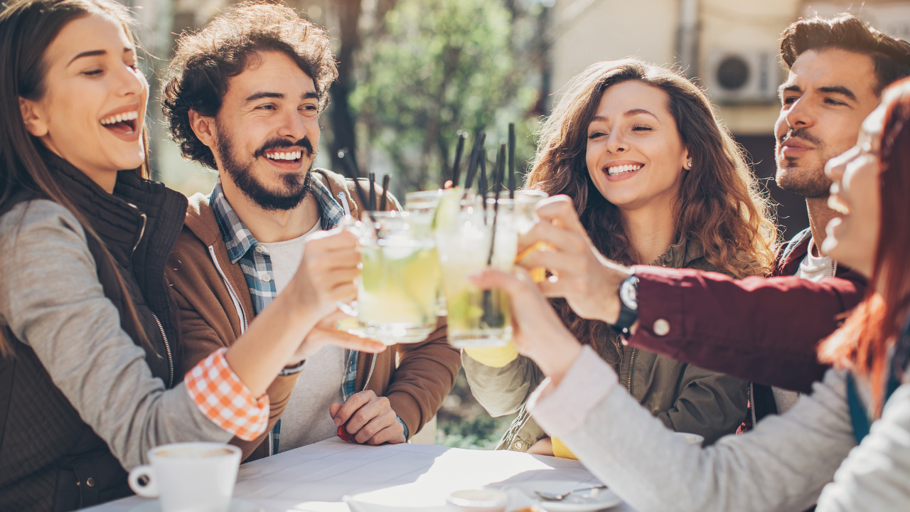 Group of friends outdoors clinking glasses with drinks, smiling and enjoying each other's company.
