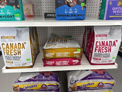 Shelf with bags of Canadian Fresh pet food, including chicken, salmon, and other flavors; assorted pet food brands and packages.