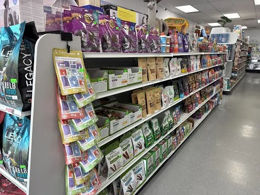 Shelves in a pet store aisle displaying various pet food and supplies, including bags of dog or cat food and treats.