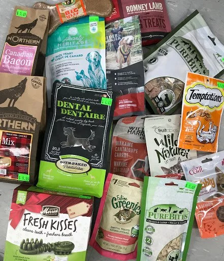 Dog treats and snacks for purchase, including various branded packages like Temptations, Pure Bites, Greenies, and other pet treats. Price tags attached on some items, displayed on a surface.