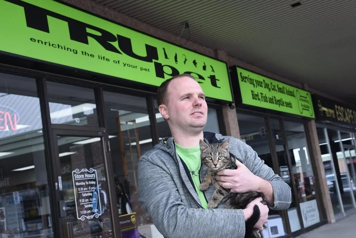 A man standing outside a pet store holding a tabby cat in his arms