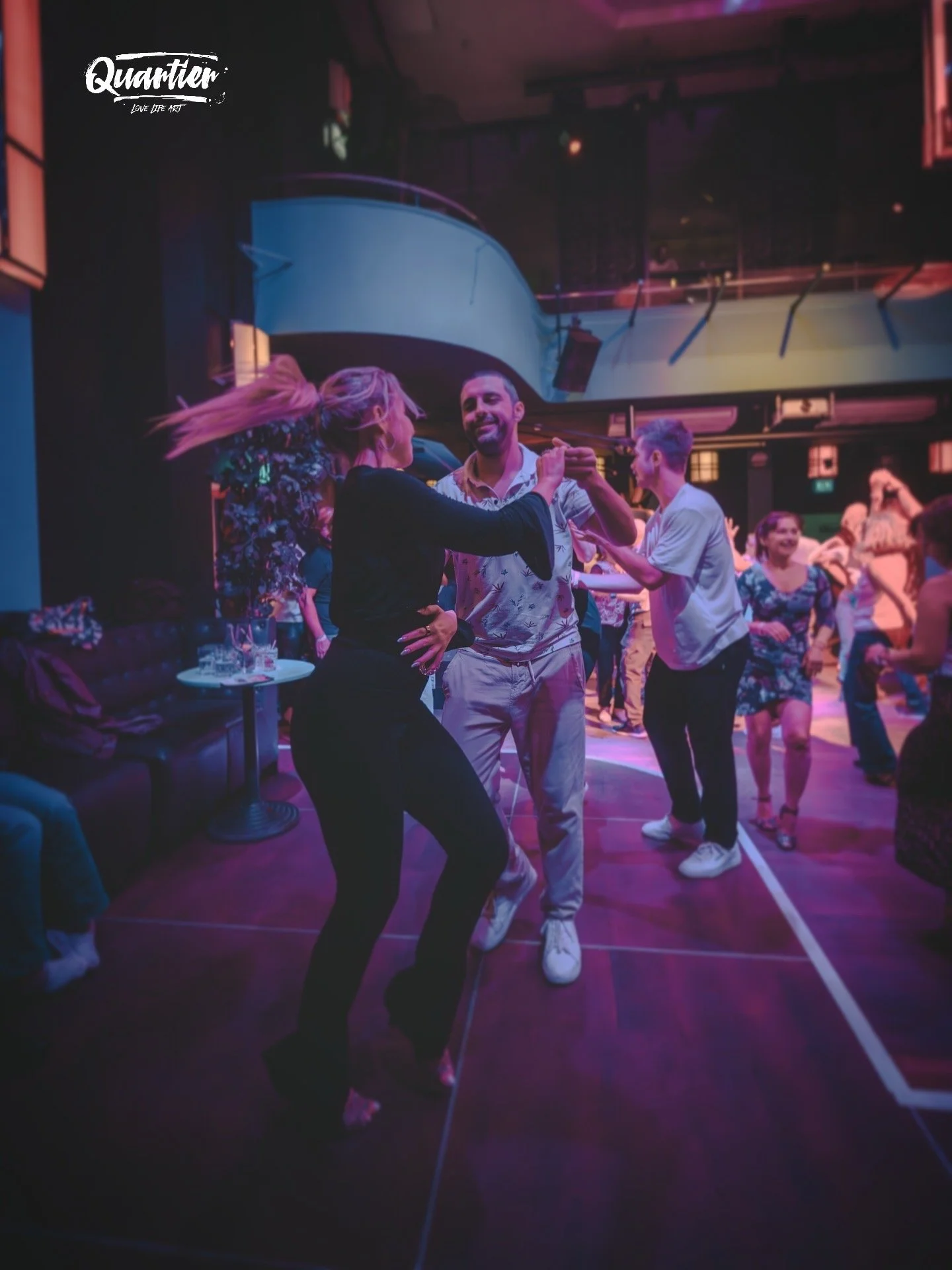 Menschen tanzen auf einer Party in einem Club mit dunkler Beleuchtung und bunten Lichtern, einige lachen und haben Spaß, während sie sich amüsieren.