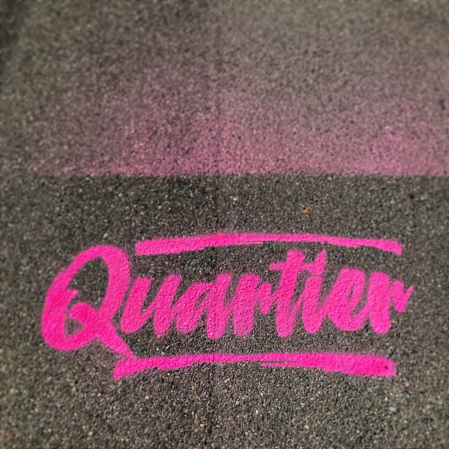 Kreidezeichnung mit dem Wort 'Quanter' in Pink auf einer Asphaltoberfläche.