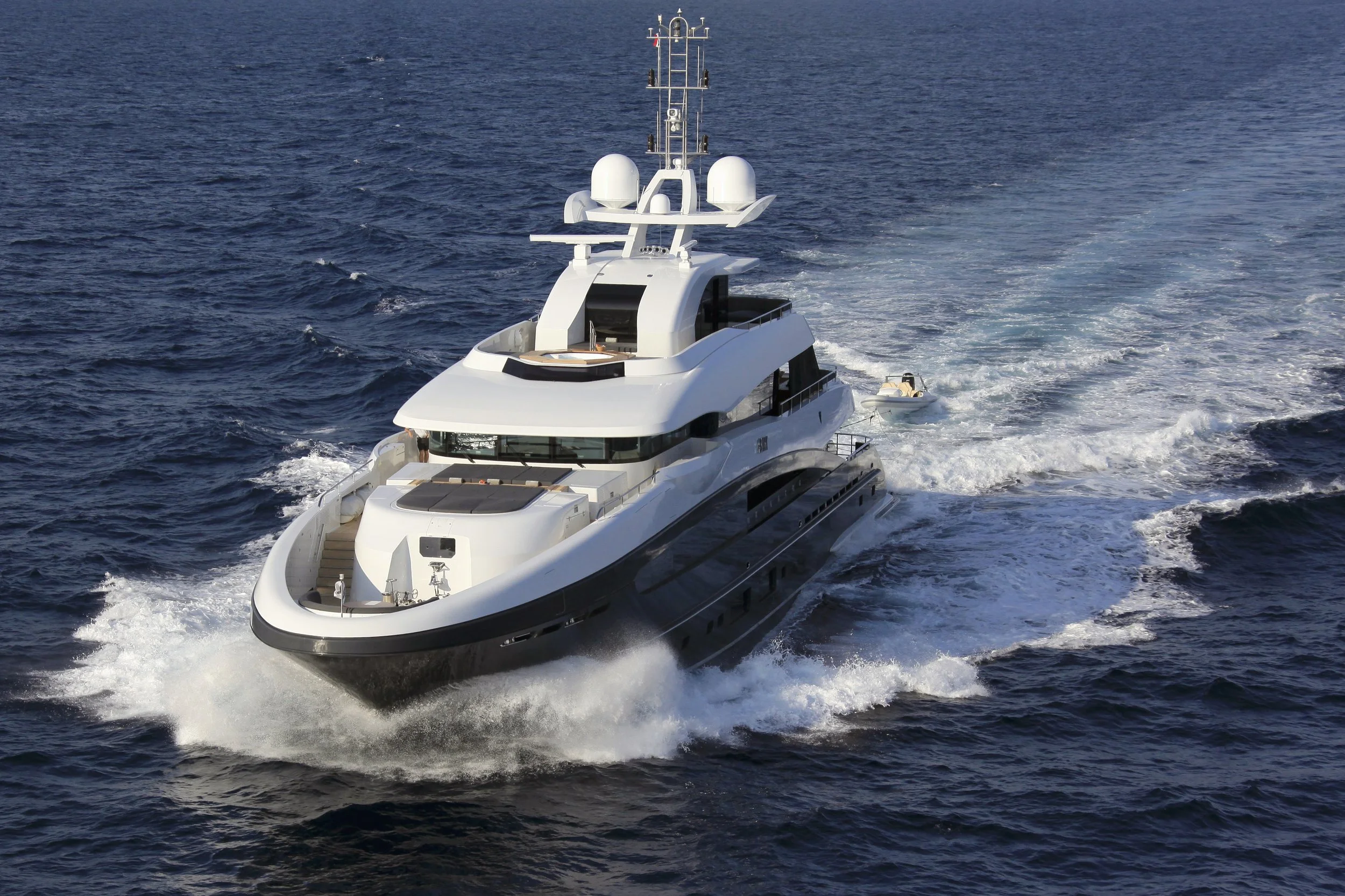 A large white yacht sailing in open water with a small boat trailing behind.