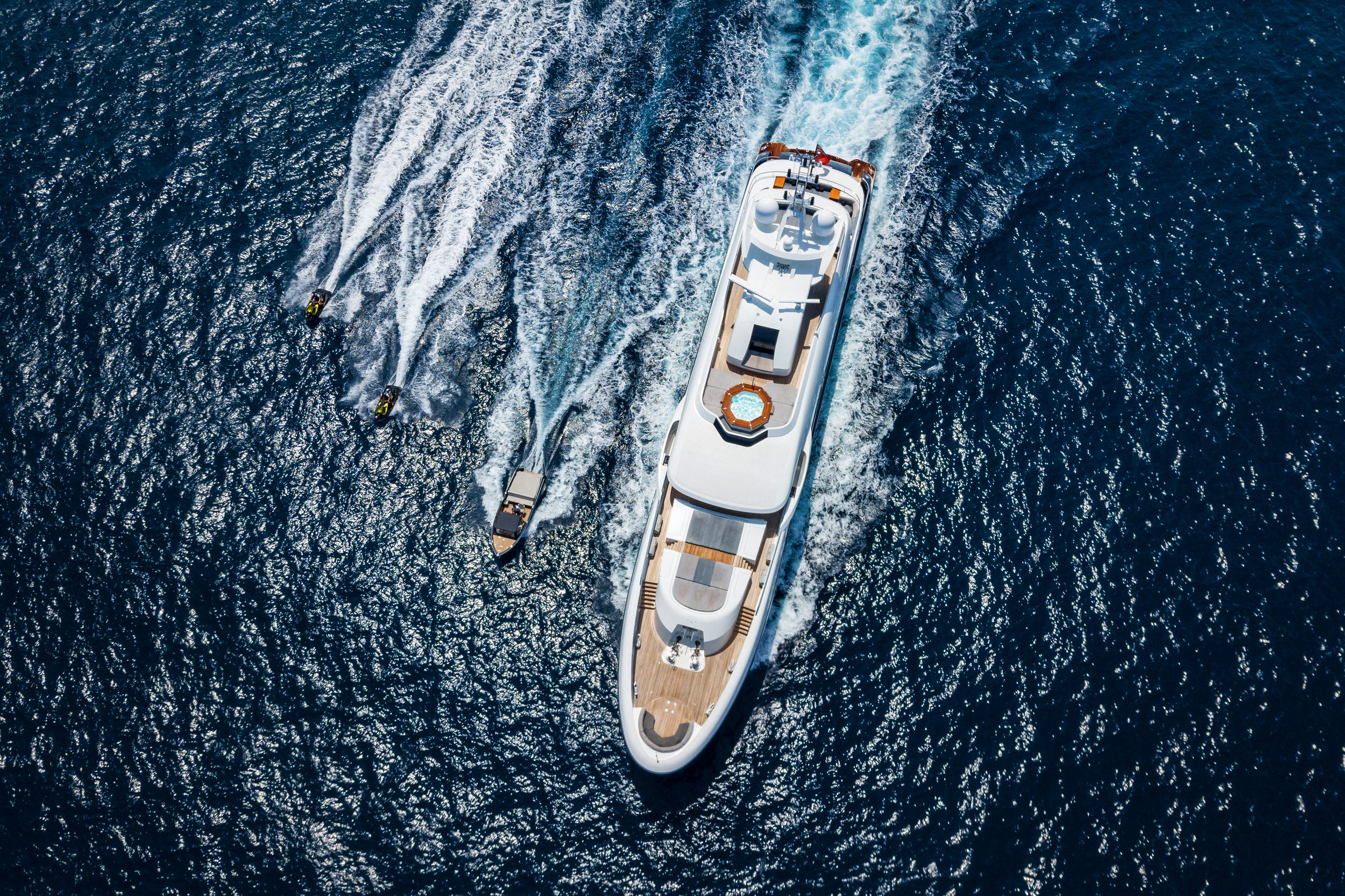 An aerial view of a large luxury yacht moving through the ocean, accompanied by two smaller boats.