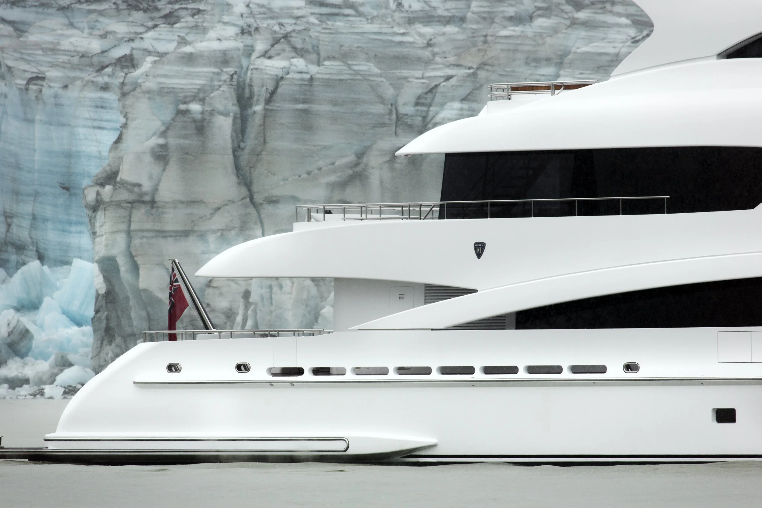 Close-up of a large luxury white yacht docked near icy glaciers, with part of a red flag visible at the stern.