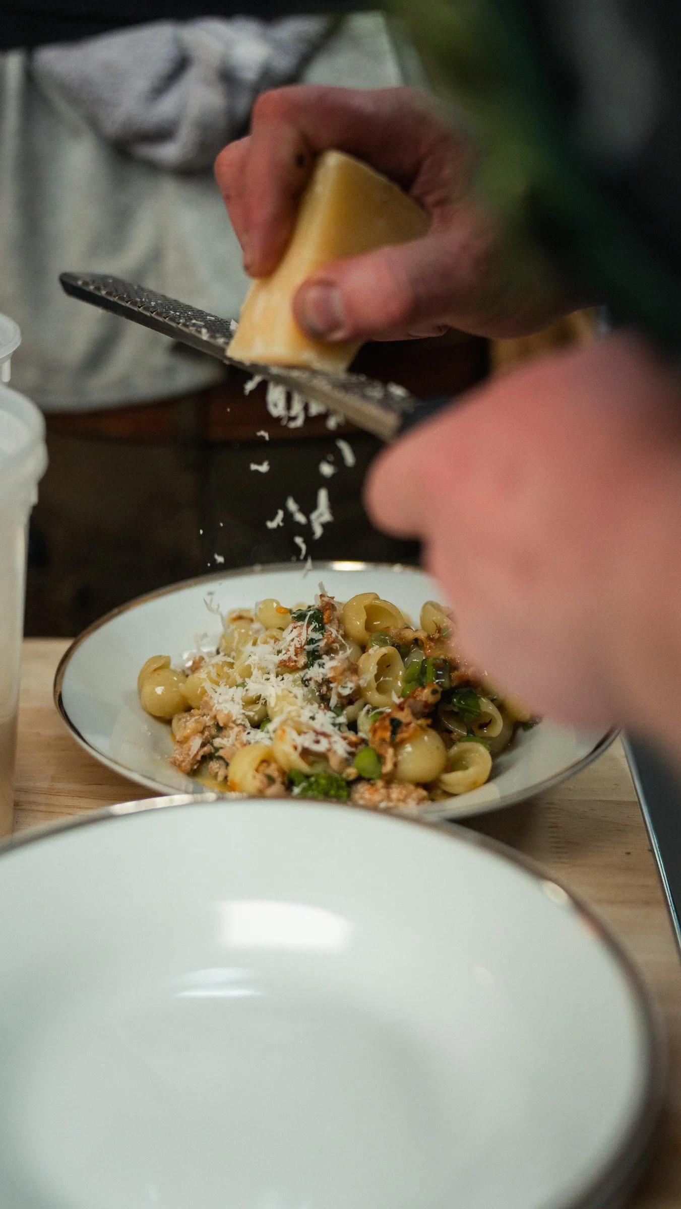 A person grating cheese over a pasta dish