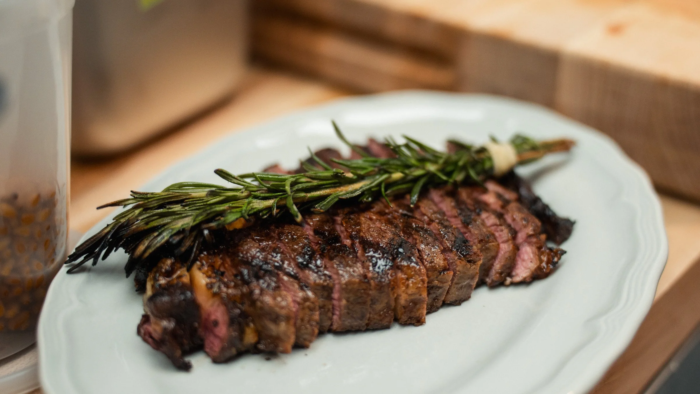 A grilled steak topped with a sprig of rosemary on a white plate.