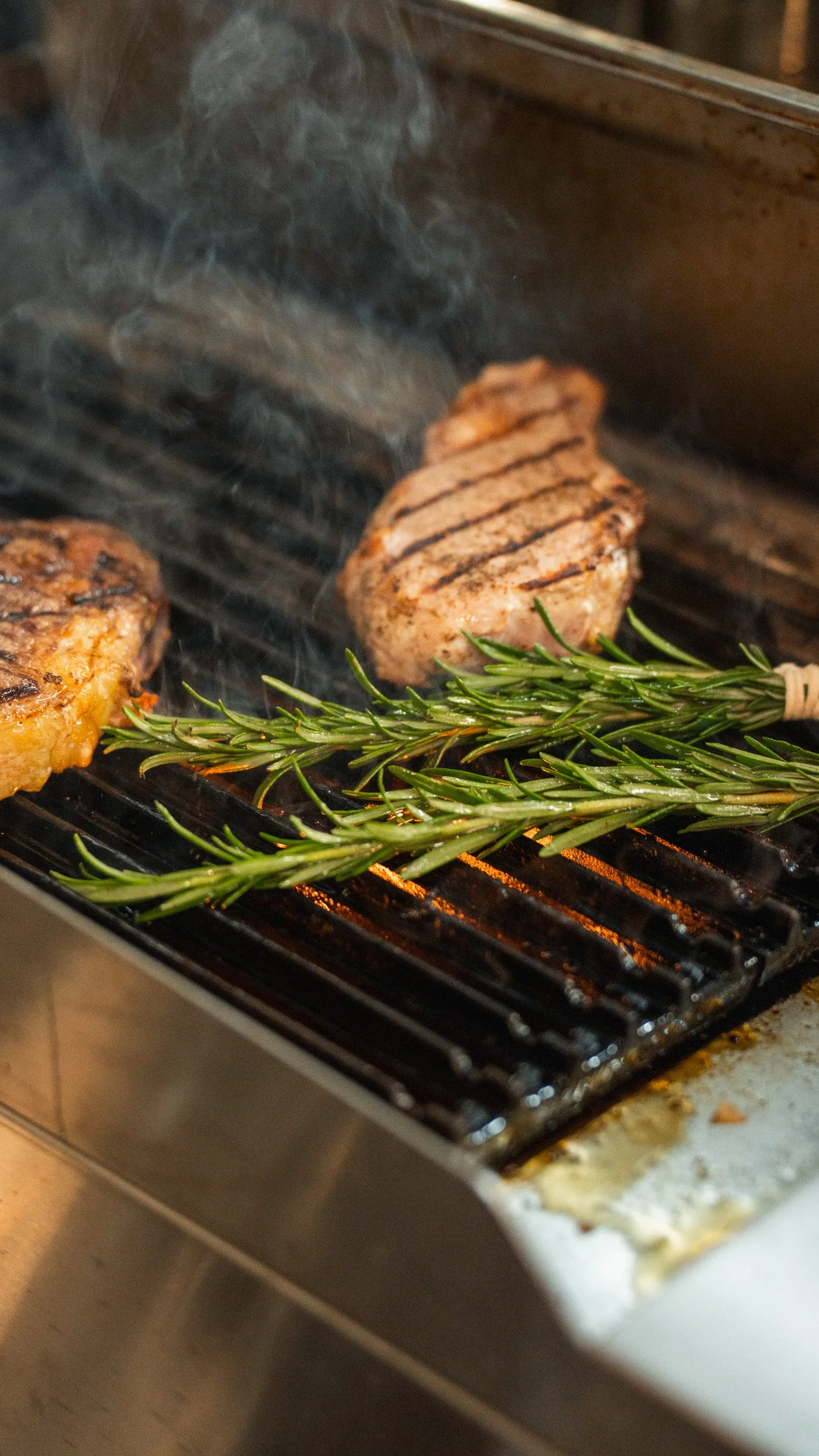Two grilled meat patties and a sprig of fresh rosemary on a barbecue grill.