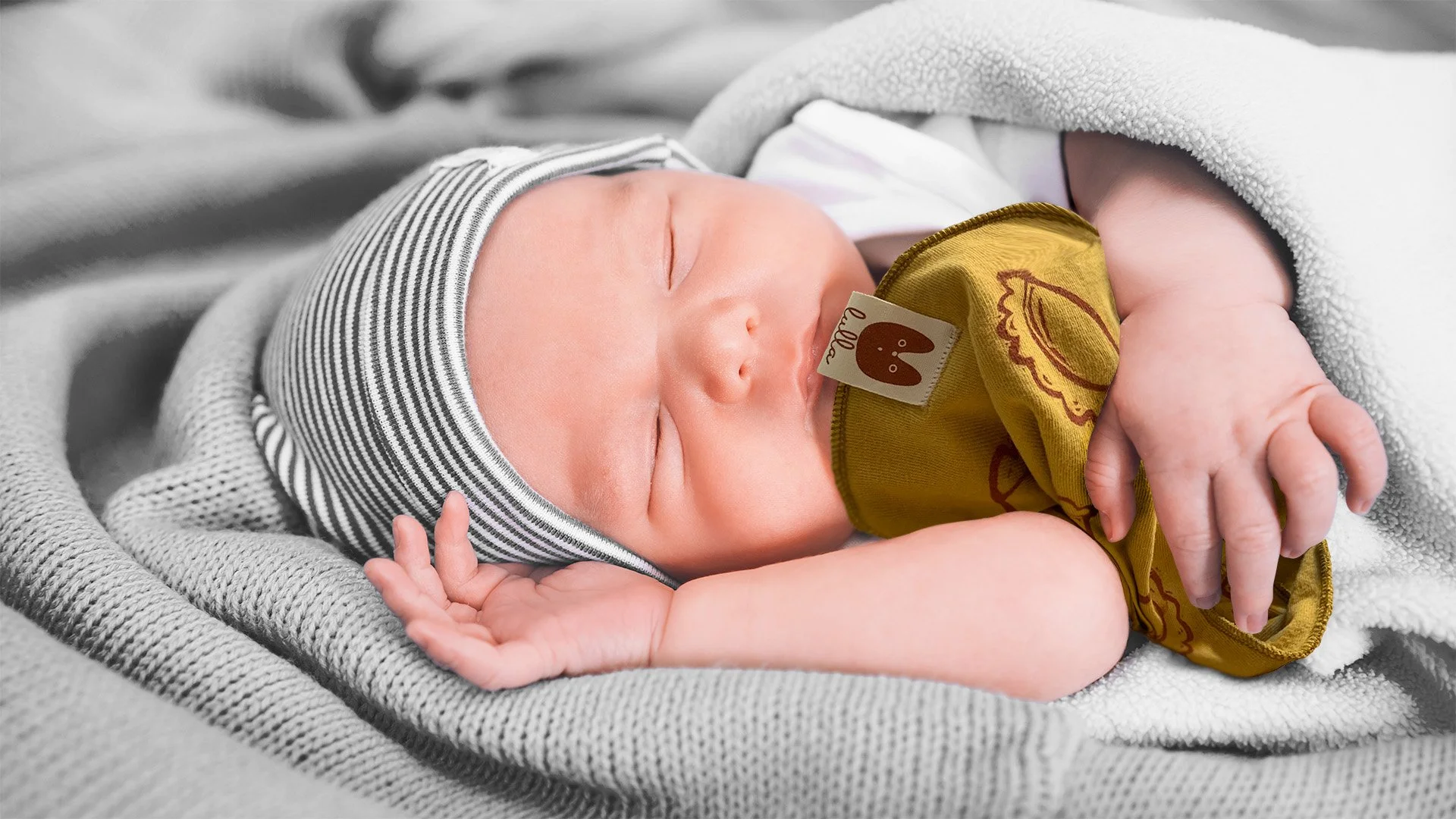 Close-up of a sleeping baby with a hat, wrapped in a blanket, hugging a lullabib