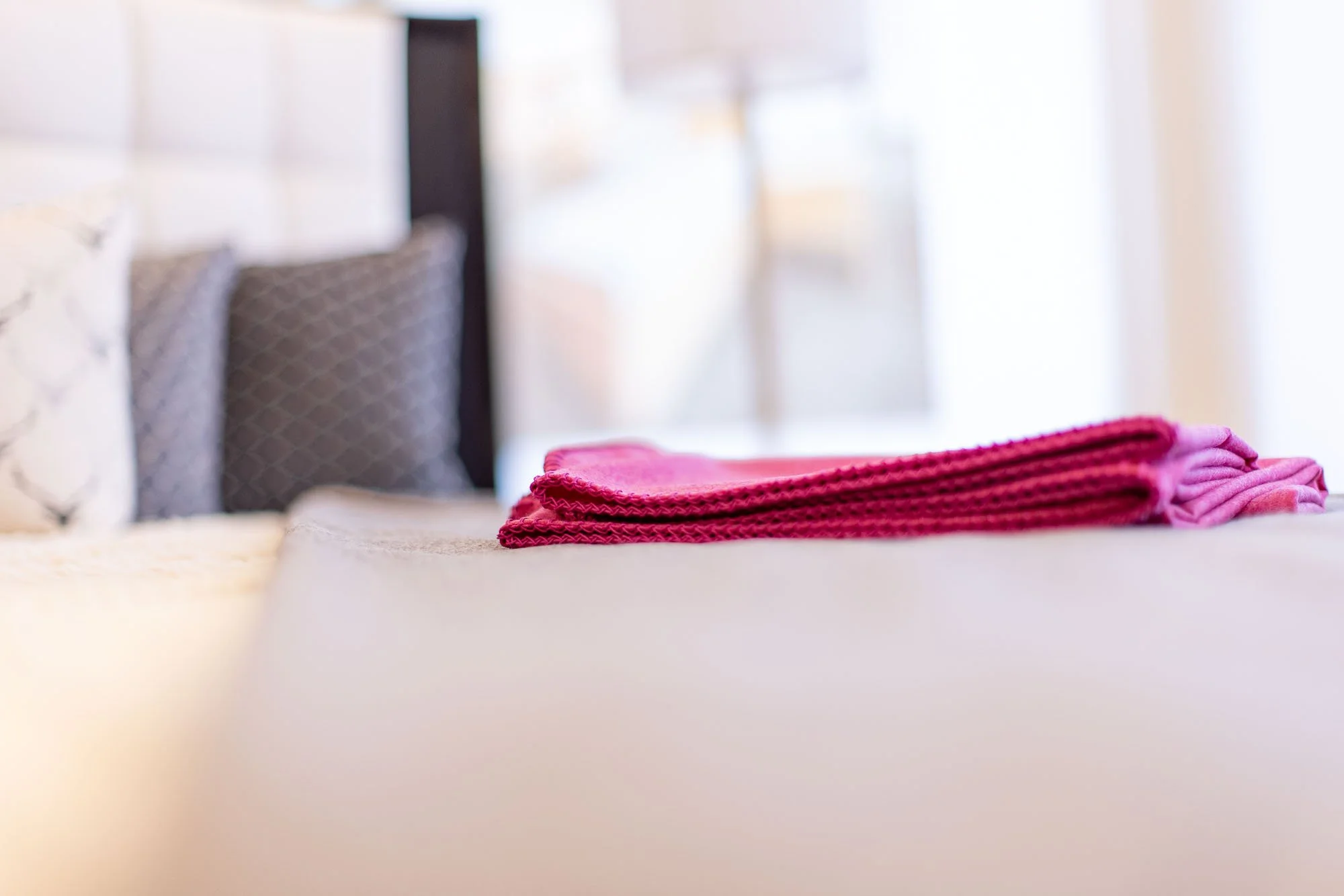 Bett mit pinker Decke vor Kopfkissen und grauen Polster auf einem weißen Bett im Schlafzimmer.
