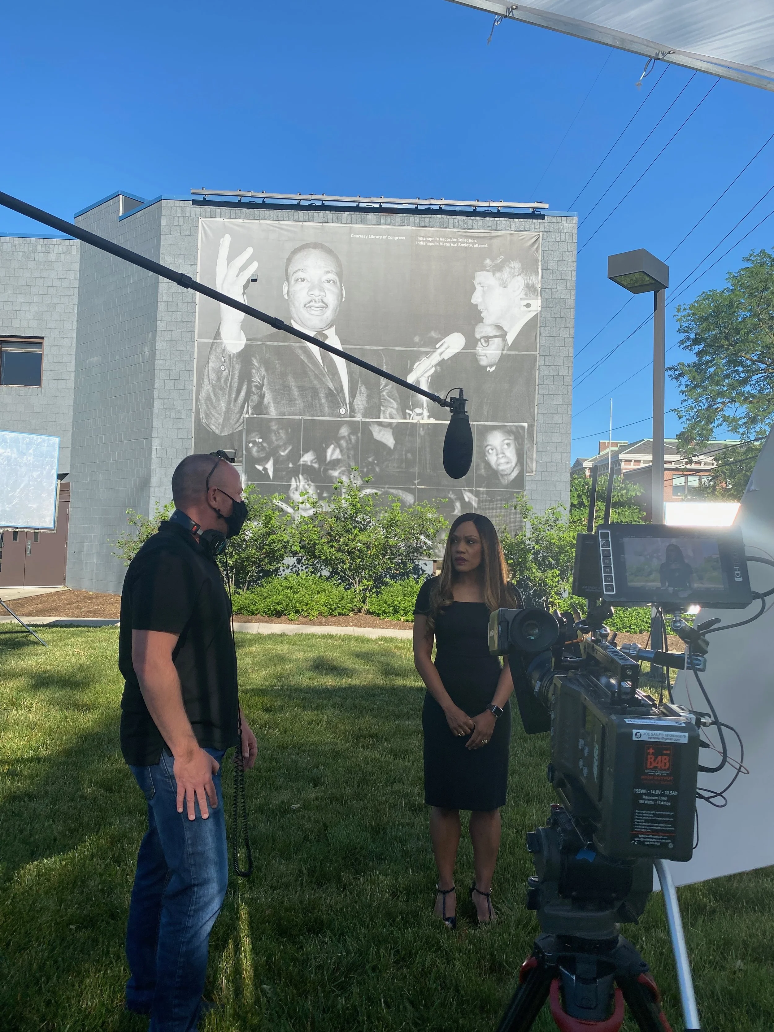Group of five diverse people standing together, one woman holding a framed certificate, smiling for a photo indoors.