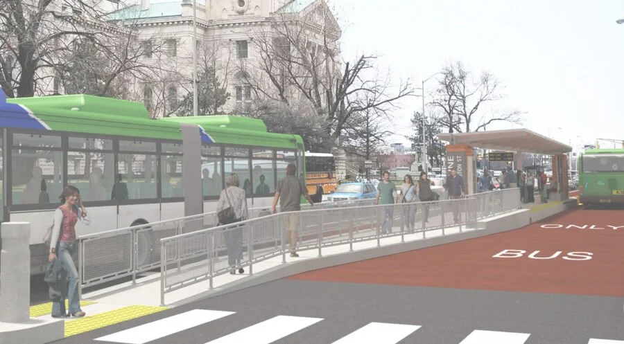 People waiting at a bus stop with a bus arriving. Crosswalk in foreground, city buildings and trees in background.