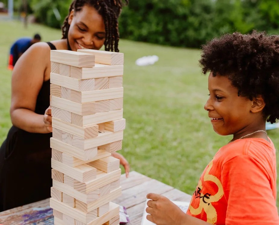 A woman and a young girl playing Jenga outdoors at a park.