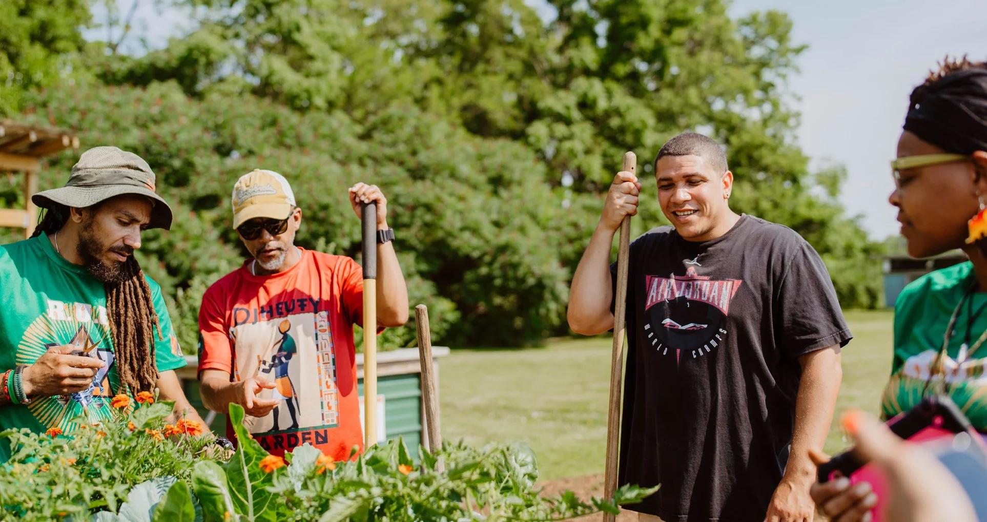 People working in a community garden on a sunny day surrounded by green trees