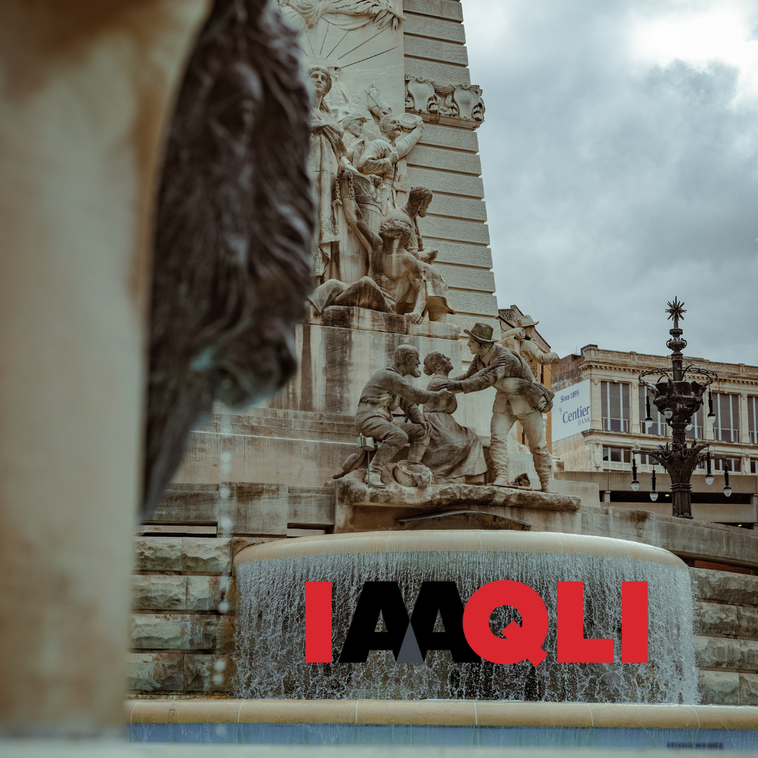 Famous city square fountain with a detailed sculpture and a large installation of the word 'IAAQLI' in red and black letters in front of water cascading from the fountain.