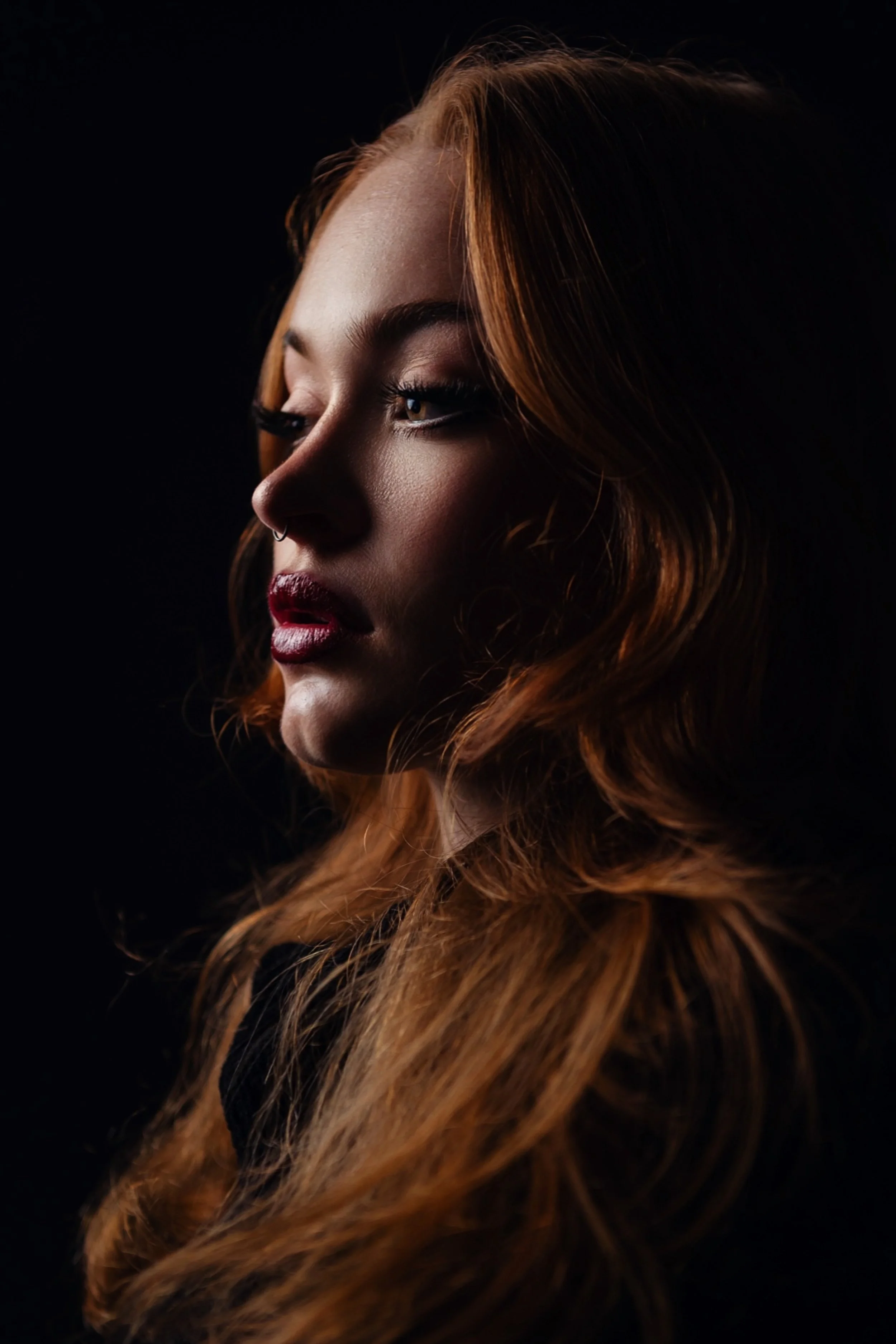 A woman with red hair and makeup against a black background.