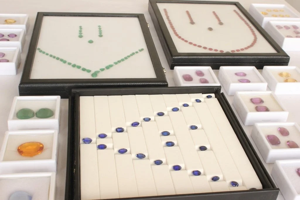 Display of various gemstone jewelry designs made with colorful gemstones, including necklaces and earrings, arranged on a table.