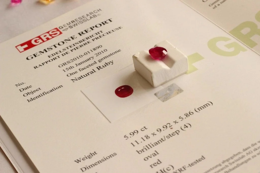 Gemstone report from the Swiss Gem Research, featuring a small brush with a red gemstone, a red gemstone, and a square white object on a report document.