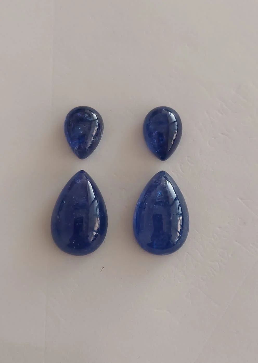 Four dark blue glass gemstones, two small teardrop-shaped at the top and two larger teardrop-shaped at the bottom, arranged in a symmetric pattern on a light-colored surface.