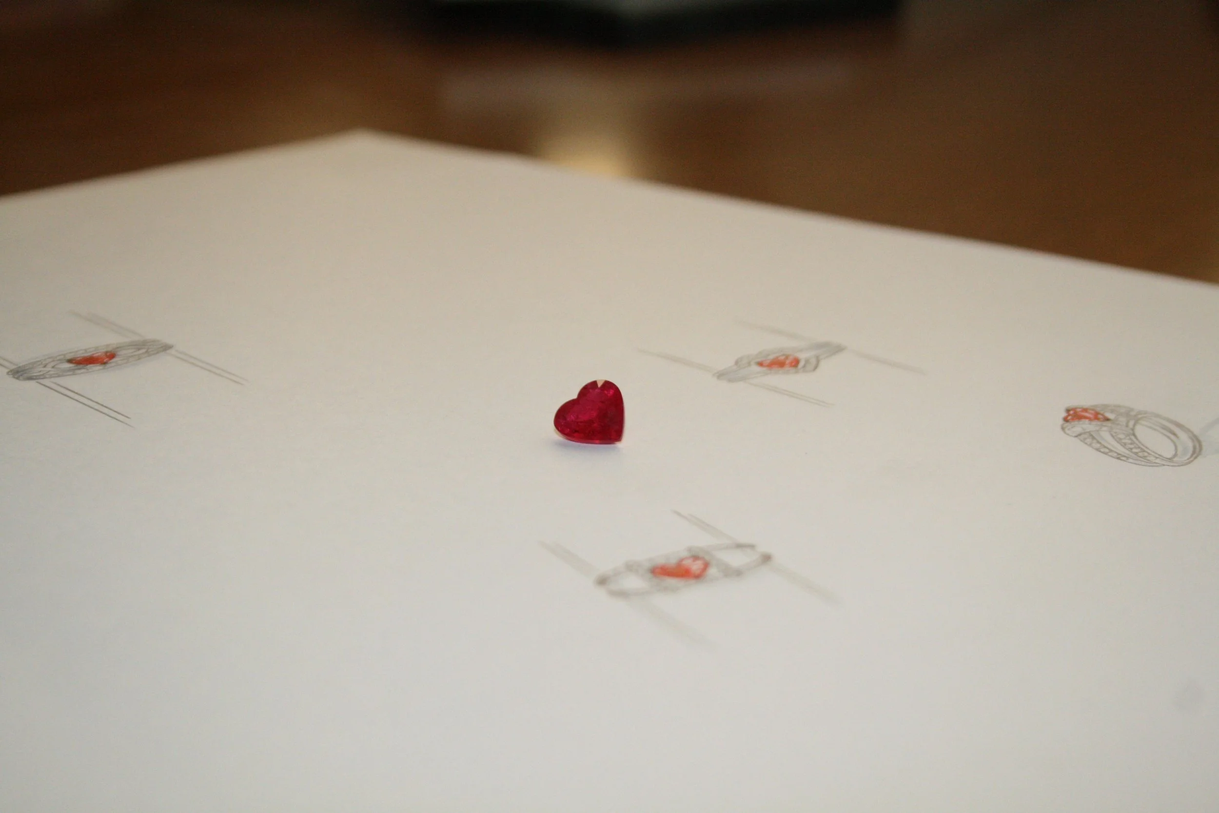 A small red heart-shaped object on a white sheet of paper with faint printed holiday-themed illustrations.