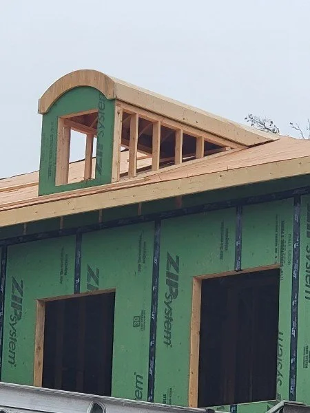 Building under construction with green siding, wooden framing, and an arched dormer on the roof.
