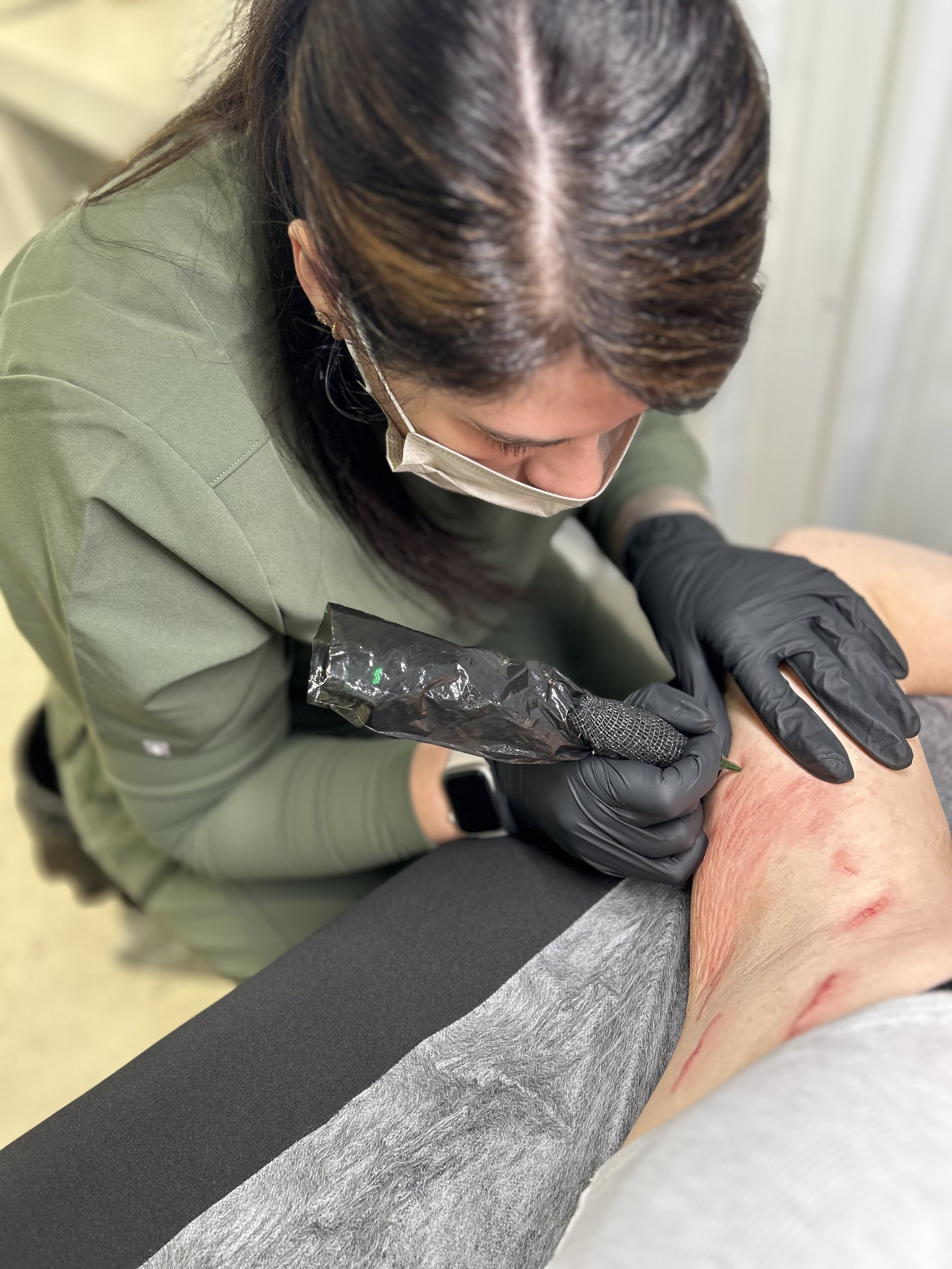 A person in gloves and a mask tattoos a leg with red marks on the skin.