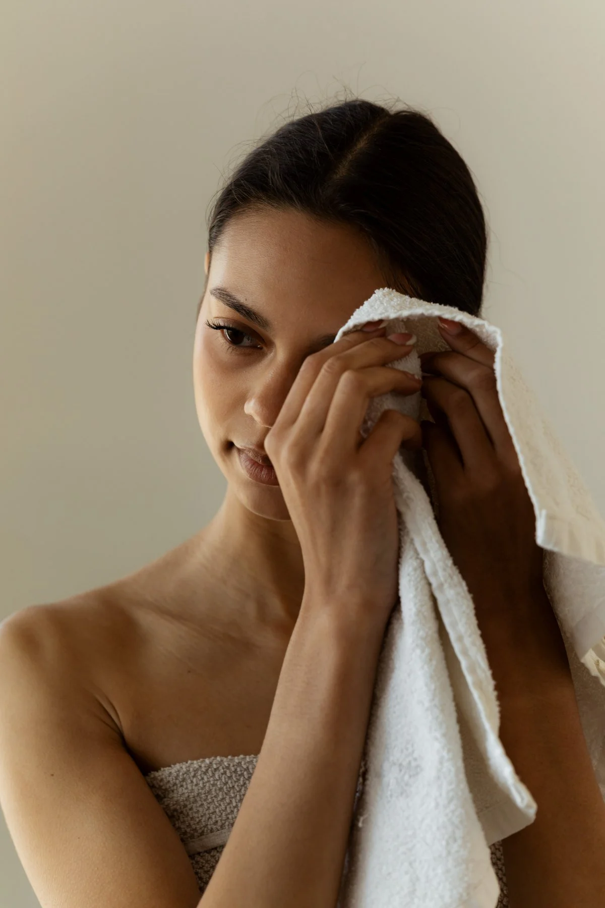 A woman wiping her face with a towel, looking down thoughtfully.