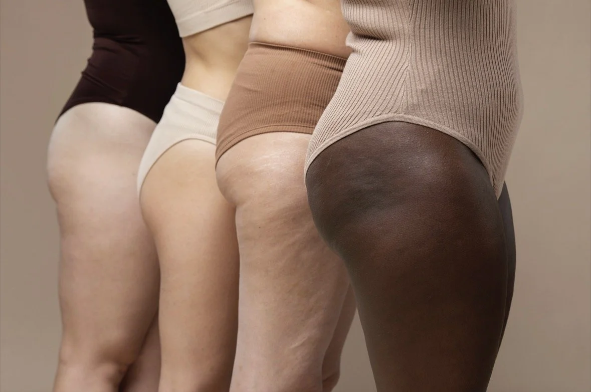 Close-up of four women's lower bodies showing different skin tones and textures, wearing beige and brown undergarments.