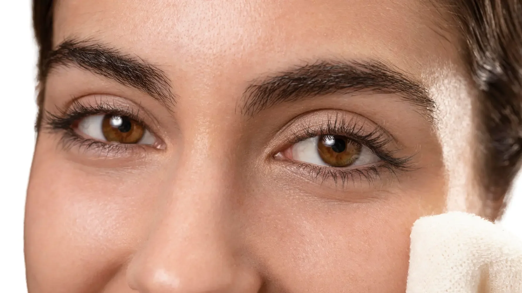 Close-up of a person's face with a focus on one eye and eyebrow, with a white sponge near the other eye, suggesting a skincare or makeup application process.